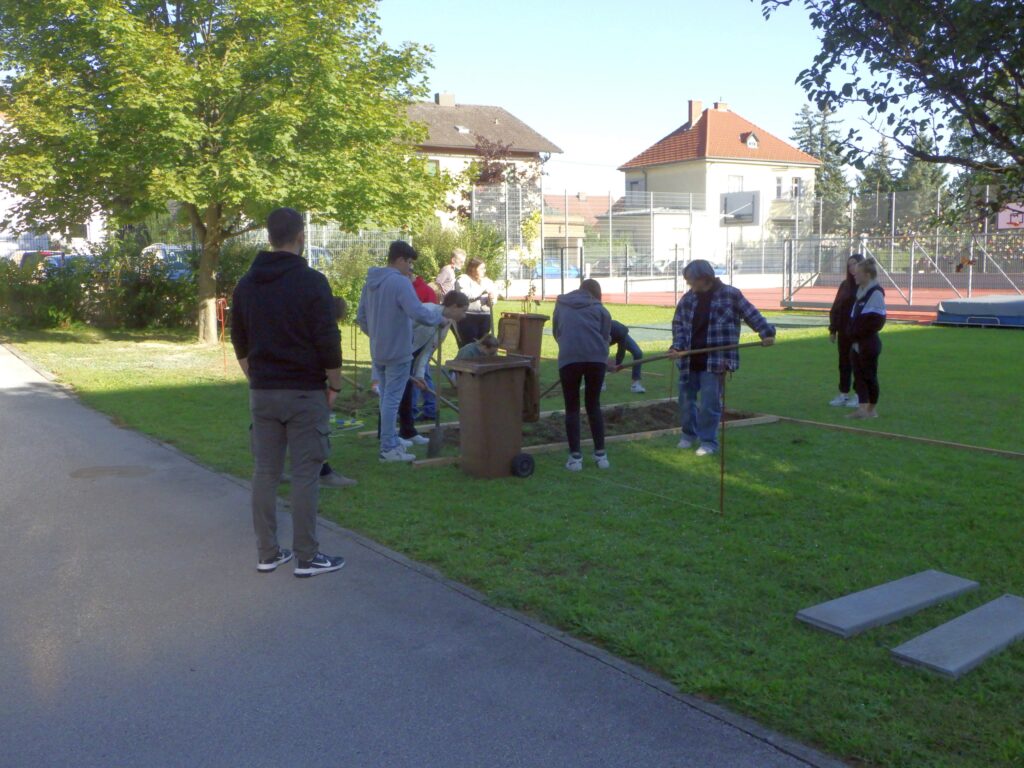 Im Bild sind Schüler*innen zu sehen, die auf einer Rasenfläche den Untergrund für ein Projekt befestigen.