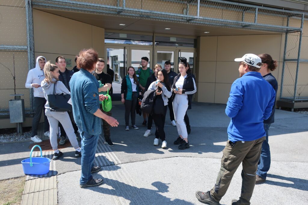 Im Bild sind Schüler*innen und Lehrpersonal zu sehen, die Grünpflegetätigkeiten besprechen