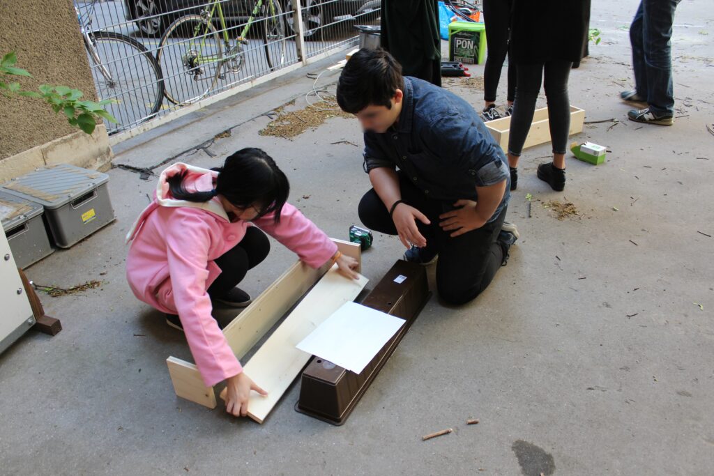 Im Bild sind zwei Schüler*innen zu sehen, die an einem Holztrog arbeiten.