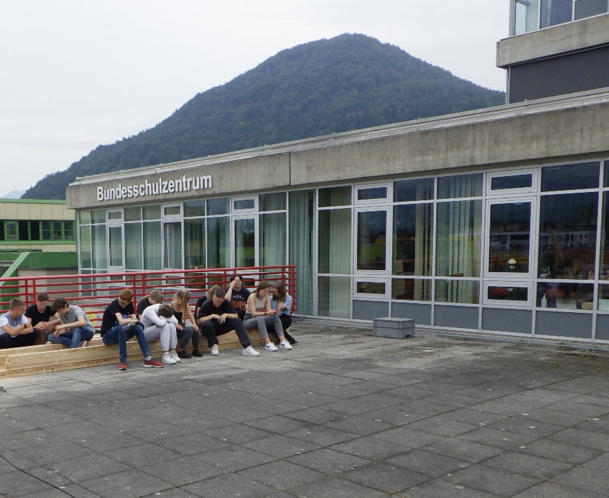 Im Bild sind Schüler*innen auf einer Beton-Terrasse vor der Schule zu sehen.