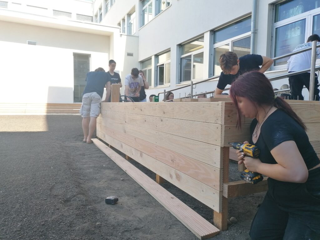 Im Bild sind Schüler*innen zu sehen, die ein Hochbeet im Schulgarten bauen.