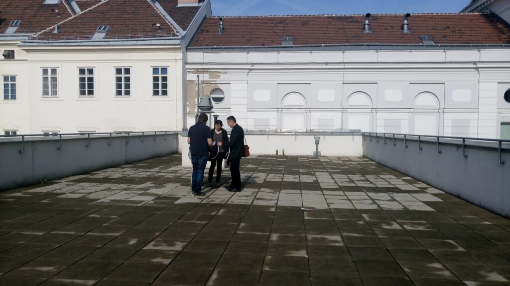 Im Bild ist eine leere Dachterrasse zu sehen, auf der sich Personen beraten.