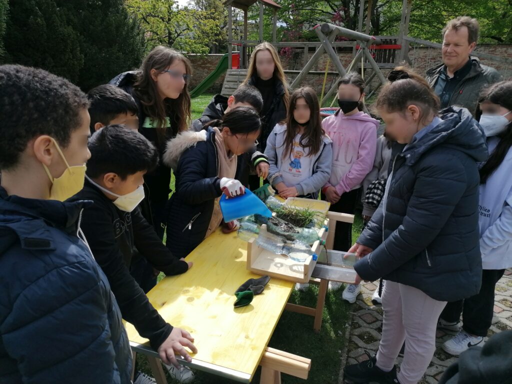 Im Bild sind Schüler*innen zu sehen, die einen Versuch zu Bodenerosion durchführen.