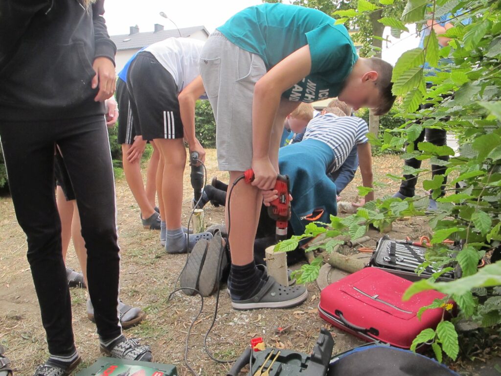 Im Bild sind Schüler*innen zu sehen, die Arbeiten für ein Insektenhotel durchführen.