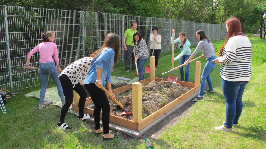 Im Bild sind Schüler*innen zu sehen, die ein Hochbeet im Garten aufbauen.